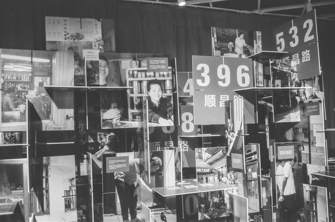 grayscale photo of man in white shirt standing near glass wall