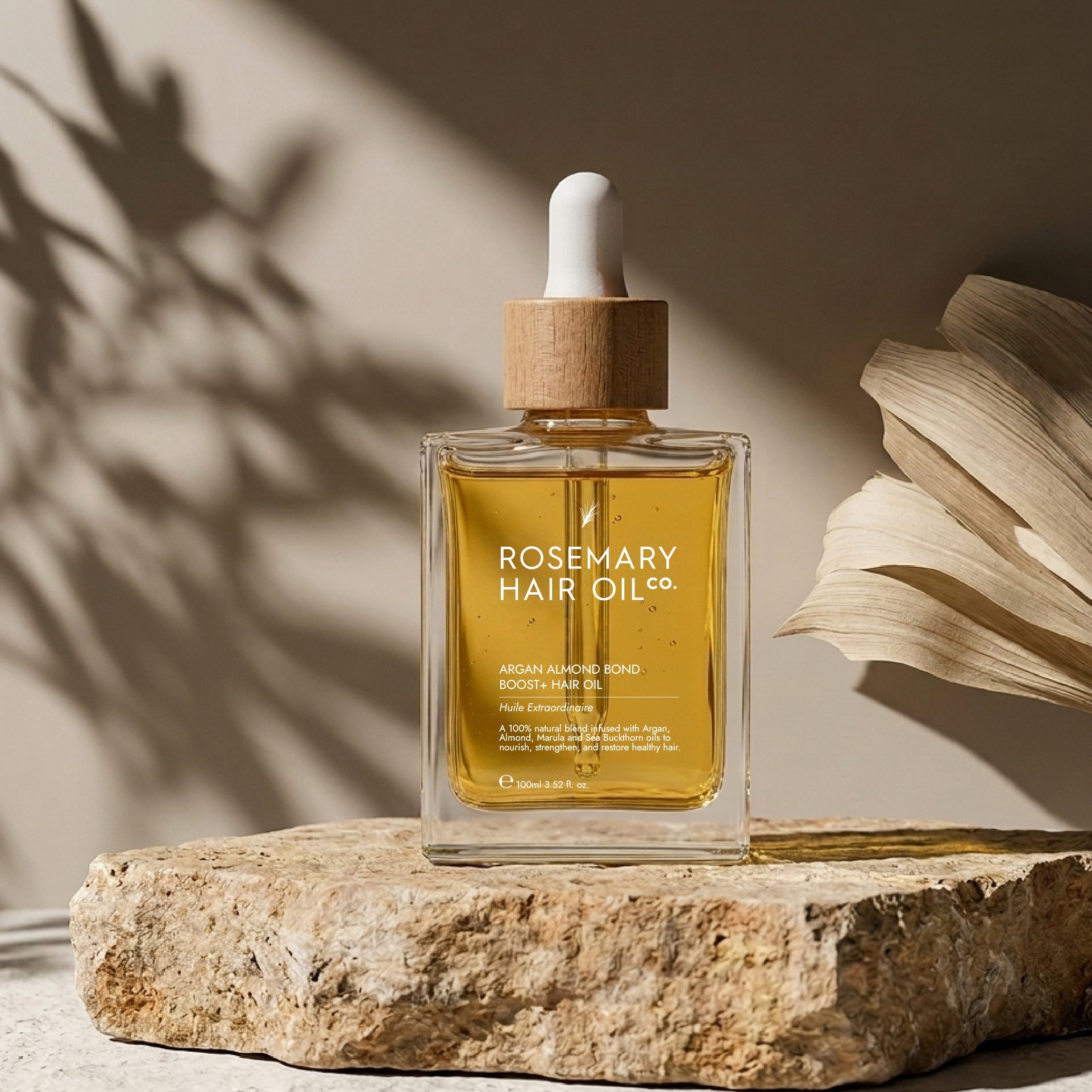 Rosemary hair oil bottle with dropper on a stone surface with natural light. Rosemary hair oil, argan, almond, bond, boost, hair growth, coconut oil, healthier, fuller-looking hair, stimulate, regrowth, hair thinning, natural, 100ml, 